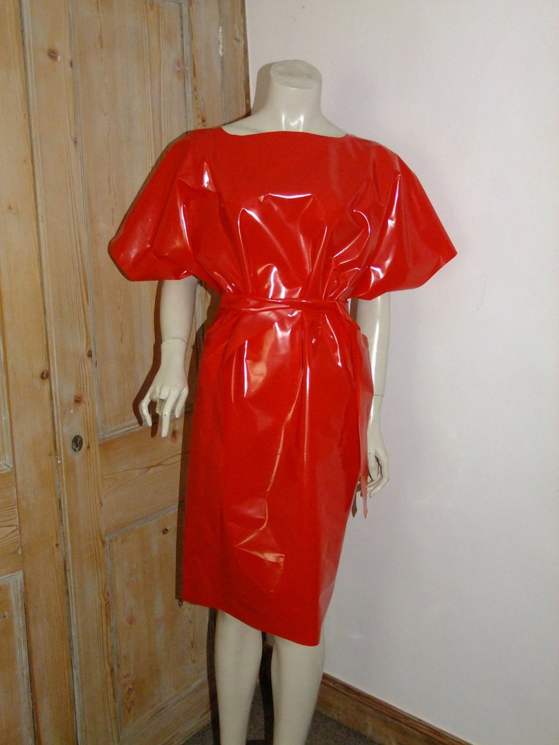 K&ouml;nnte beinhalten: Ein rotes, gl&auml;nzendes, &auml;rmelloses Kleid mit einer taillierten Taille und einem einfachen, abgerundeten Ausschnitt.