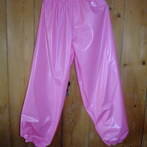 May include: Pink shiny pants with a gathered elastic waistband and gathered cuffs. The pants are made of a smooth, silky material.