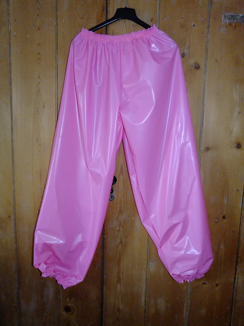 May include: Pink shiny pants with a gathered elastic waistband and gathered cuffs. The pants are made of a smooth, silky material.