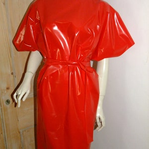 K&ouml;nnte beinhalten: Ein leuchtend rotes, gl&auml;nzendes, &auml;rmelloses Kleid mit einem Bindeg&uuml;rtel. Das Kleid ist aus einem glatten, gl&auml;nzenden Material gefertigt.
