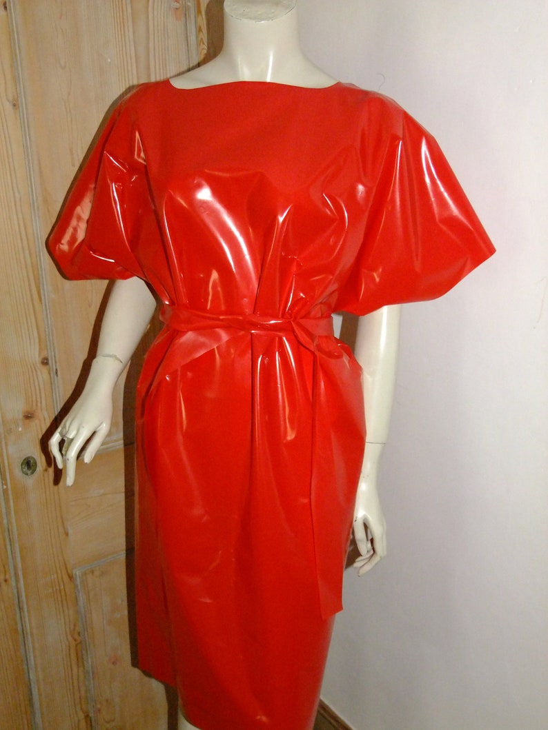 K&ouml;nnte beinhalten: Ein leuchtend rotes, gl&auml;nzendes, &auml;rmelloses Kleid mit einem Bindeg&uuml;rtel. Das Kleid ist aus einem glatten, gl&auml;nzenden Material gefertigt.