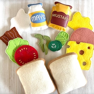 May include: Felt food set for pretend play, featuring a sandwich with bread, lettuce, tomato, bacon, cheese, and a slice of ham.  The set also includes condiments, mustard and mayonnaise, and cucumber slices.