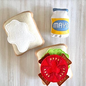 May include: Felt food play set with two pieces of bread, a tomato, lettuce, and a bottle of mayonnaise labeled "MAYO".