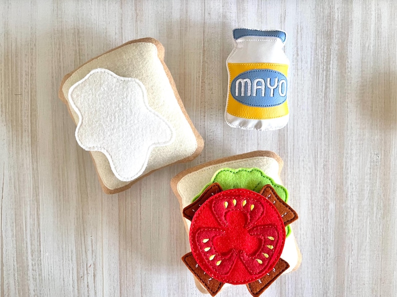 May include: Felt food play set with two pieces of bread, a tomato, lettuce, and a bottle of mayonnaise labeled "MAYO".