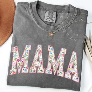 May include: Gray t-shirt with a floral print "MAMA" design. The shirt is made of a soft, comfortable fabric.