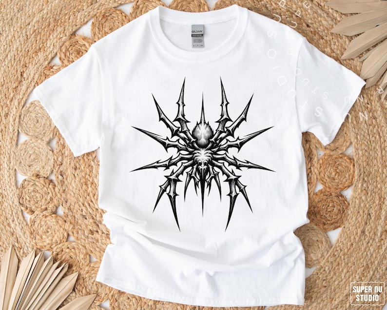May include: White t-shirt featuring a detailed black and gray spider graphic. The spider design has sharp, spiky legs and a central body, creating a striking contrast against the white fabric. The shirt is a classic crew neck style.