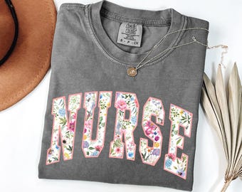 May include: Gray t-shirt with a floral print of the word "NURSE" in pink.