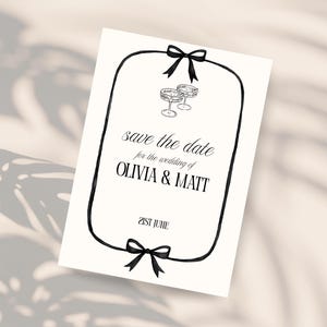 May include: A white card with black text and a black border, featuring the words "save the date for the wedding of OLIVIA & MATT" and "21st June." Two champagne glasses are drawn at the top, and black bows are at the top and bottom.