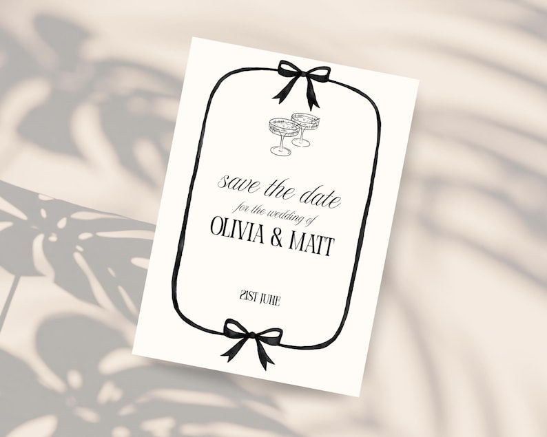 May include: A white card with black text and a black border, featuring the words "save the date for the wedding of OLIVIA & MATT" and "21st June." Two champagne glasses are drawn at the top, and black bows are at the top and bottom.