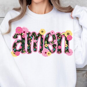 Op de afbeelding: Wit sweatshirt met een bloemenontwerp dat het woord "amen" spelt.