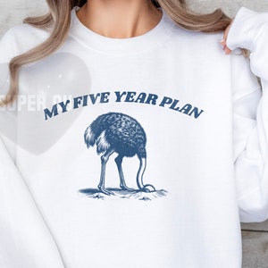K&ouml;nnte beinhalten: Wei&szlig;er Pullover mit einem blauen Aufdruck einer Strau&szlig; mit dem Kopf im Sand und dem Text "My Five Year Plan".