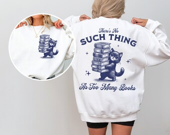 May include: White sweatshirt with a blue cat carrying a stack of books. The text on the sweatshirt reads "There's No Such Thing As Too Many Books".