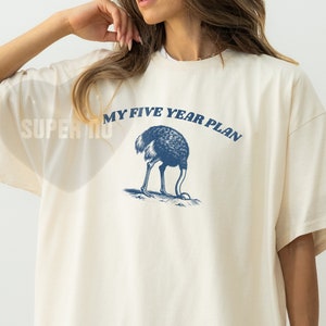 K&ouml;nnte beinhalten: Ein wei&szlig;es T-Shirt mit einer blauen Grafik einer Strau&szlig;envogel mit dem Text "My Five Year Plan" darauf.
