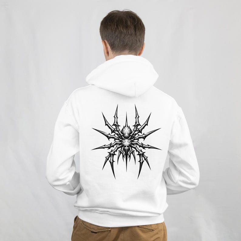 May include: White hoodie featuring a large, detailed black and gray spider design on the back. The spider graphic has a spiky, intricate design. The hoodie has a hood and long sleeves. The person is facing away from the camera.