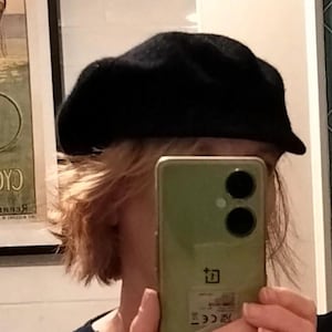 Peut inclure: Un béret noir uni doté d'une calotte arrondie et d'une visière courte et structurée. Le chapeau présente une texture douce et feutrée, se posant sur la tête pour couvrir le haut du front avec une silhouette épurée et sans aucun motif.
