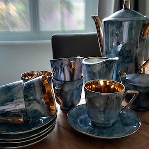 Peut inclure: Un service à thé comprenant une théière haute, un pot à lait, un sucrier et plusieurs tasses avec soucoupes assorties. Chaque pièce présente un motif marbré bleu et blanc avec une finition brillante et des accents dorés.