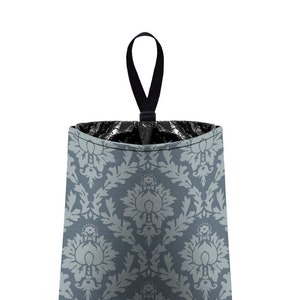 May include: A gray and white patterned fabric trash can with a black hanging strap. The trash can is designed to hang on a door or wall.