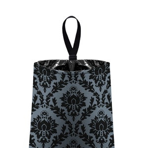 May include: A gray and black patterned fabric trash can with a black hanging loop. The trash can has a damask pattern.