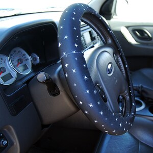 May include: A black steering wheel cover with a white star pattern. The cover is made of a soft, comfortable material and is designed to improve grip and comfort while driving.