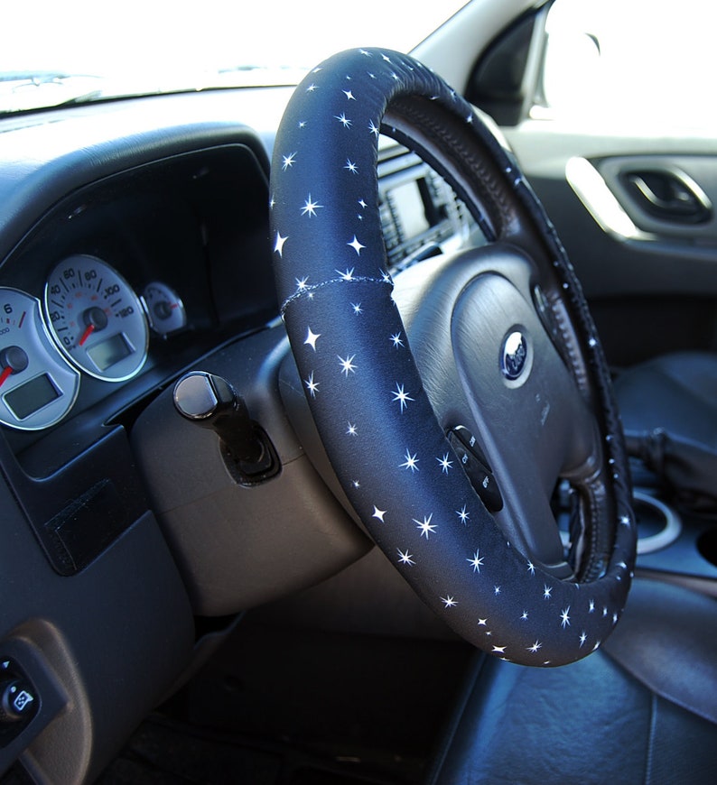 May include: A black steering wheel cover with a white star pattern. The cover is made of a soft, comfortable material and is designed to improve grip and comfort while driving.