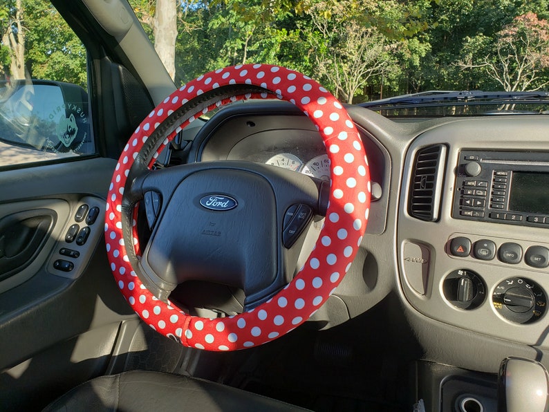 Pu&ograve; includere: Coprivolante rosso con pois bianchi. Il coprivolante &egrave; installato su un volante Ford all'interno di un veicolo. L'interno dell'auto &egrave; visibile, compreso il cruscotto e i sedili.