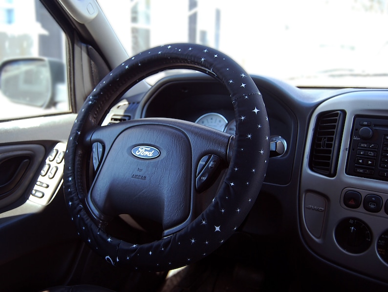 May include: A black steering wheel with a blue and white star pattern cover. The steering wheel has a silver Ford logo and the word "Escape" written below it.