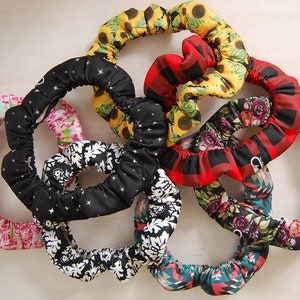 May include: A set of eight colorful fabric covered hair ties. The hair ties are in a variety of patterns, including floral, plaid, and geometric designs.