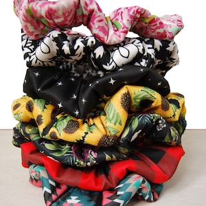 May include: A stack of eight colorful scrunchies with various patterns, including floral, geometric, and abstract designs. The scrunchies are made of soft fabric and are perfect for holding hair in place.