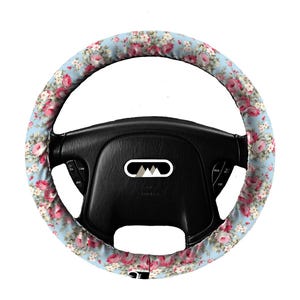 May include: A black steering wheel with a light blue floral steering wheel cover. The cover features a pattern of pink and white roses. The steering wheel has buttons and a logo in the center.