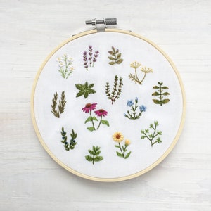 May include: A white embroidery hoop with a variety of green, yellow, pink, and blue embroidered flowers and plants.