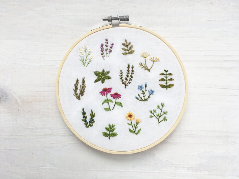 May include: A white embroidery hoop with a variety of green, yellow, pink, and blue embroidered flowers and plants.