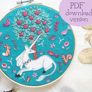 May include: Embroidered hoop art featuring a white unicorn lying under a green apple tree with pink flowers and red birds on a turquoise background.