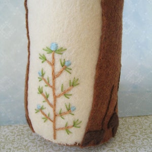May include: A brown felt tree stump with a white felt section and an embroidered green tree with blue berries.