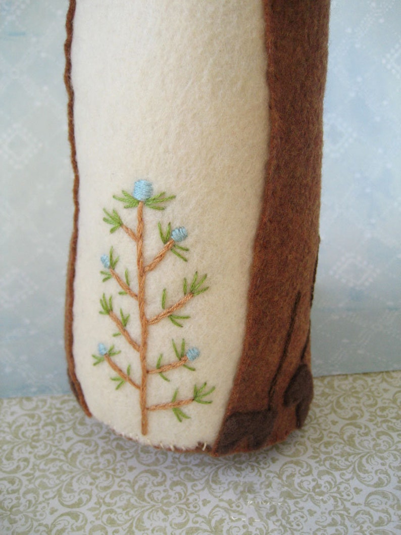 May include: A brown felt tree stump with a white felt section and an embroidered green tree with blue berries.