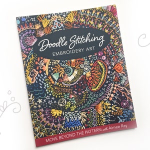 May include: A book titled "Doodle Stitching: Embroidery Art" with a colorful embroidered design on the cover. The book's subtitle is "Move Beyond the Pattern" with Aimee Ray.