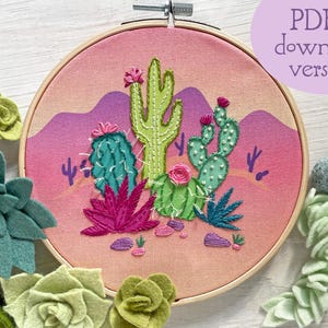 May include: Embroidered cactus scene in a wooden hoop. The design features various cacti, pink flowers, and desert landscape elements. The background is a gradient of pink and purple. The text "PDF download version" is in a purple circle.