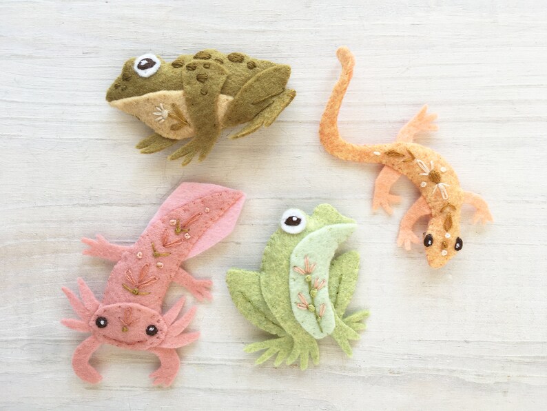 Pu&ograve; includere: Quattro figurine di animali in feltro: una rana verde, un axolotl rosa, una rana marrone e una lucertola arancione. Ogni figurina &egrave; decorata con dettagli ricamati ed &egrave; un artigianato unico fatto a mano.
