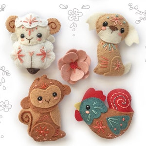 May include: Five felt animal ornaments, including a sheep, dog, monkey, rooster, and a pink flower. The animals are embroidered with colourful details and have a whimsical, cartoonish style.