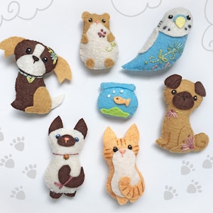 May include: A collection of handmade felt pet ornaments, including a dog, hamster, parakeet, fishbowl, pug, cat, and Siamese cat. Each ornament is crafted with detailed stitching and colorful felt, showcasing a variety of pet designs.