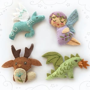 Peut inclure: Quatre ornements d'animaux en feutre : une licorne ailée bleu clair, une fée violette avec des ailes, un cerf brun avec des bois et un dragon vert avec des flammes orange.