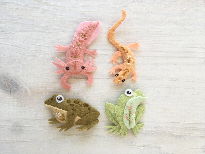 Pu&ograve; includere: Quattro figure di animali in feltro: un axolotl rosa, una lucertola marrone, una rana verde e una rana marrone. Le figure sono tutte cucite a mano e hanno dettagli ricamati.