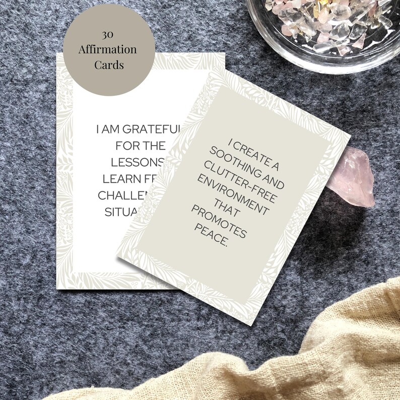 May include: Two affirmation cards with a white floral design border. The text on the first card reads "I am grateful for the lessons I learn from challenging situations." The text on the second card reads "I create a soothing and clutter-free environment that promotes peace."