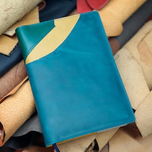 May include: A teal leather notebook with yellow and green accents. The notebook is lying on a pile of various colored leather scraps.
