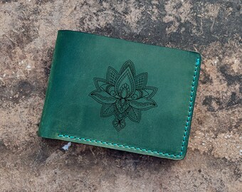 Op de afbeelding: Een groene leren portemonnee met teal stiksels en een zwart mandala-ontwerp.