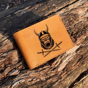 Puede incluir: Una cartera de cuero marrón con un diseño en blanco y negro de un gorila con un casco vikingo y sosteniendo espadas cruzadas.
