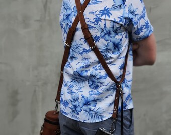 May include: A person wearing a white and blue floral shirt with a brown leather camera strap. The strap is attached to a brown leather camera bag and a silver camera.