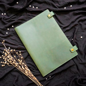 May include: A green leather folder with brass accents on a black fabric background.