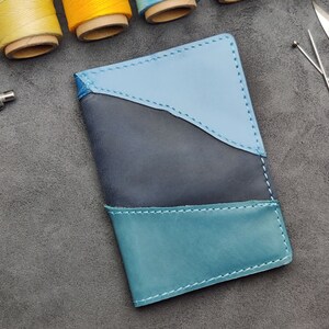Könnte beinhalten: Ein blauer, türkisfarbener und schwarzer Leder-Reisepass-Etui mit genähten Kanten.