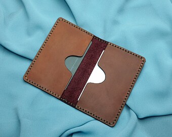 Può includere: Portacarte in pelle fatto a mano, marrone e bordeaux. Il portafoglio presenta più fessure per carte ed è cucito con un filo a contrasto. All'interno è visibile una carta con la scritta "Universal Bank".