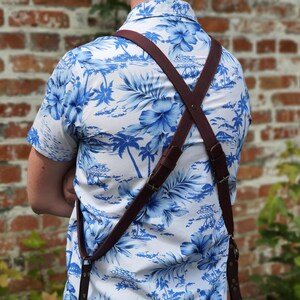 May include: A person wearing a white shirt with a blue floral pattern and a brown leather camera strap. The strap is worn across the chest and back, with the ends secured to the front of the shirt.